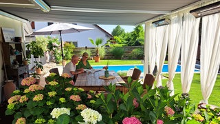 Claudia Falkenstein und Frank Stahl sitzen auf ihrer Terrasse, im Hintergrund ist der Pool.