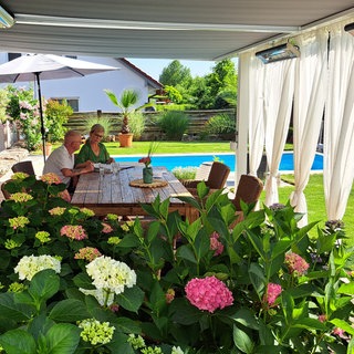 Claudia Falkenstein und Frank Stahl sitzen auf ihrer Terrasse, im Hintergrund ist der Pool.