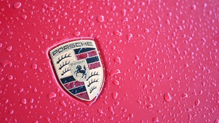 Regentropfen auf einem roten Auto mit Porsche-Logo. Der Autobauer verkauft im ersten Halbjahr 2025 weniger Autos. (Symbolbild)