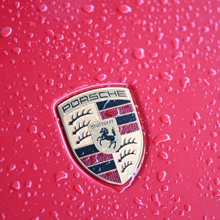 Regentropfen auf einem roten Auto mit Porsche-Logo. Der Autobauer verkauft im ersten Halbjahr 2025 weniger Autos. (Symbolbild)