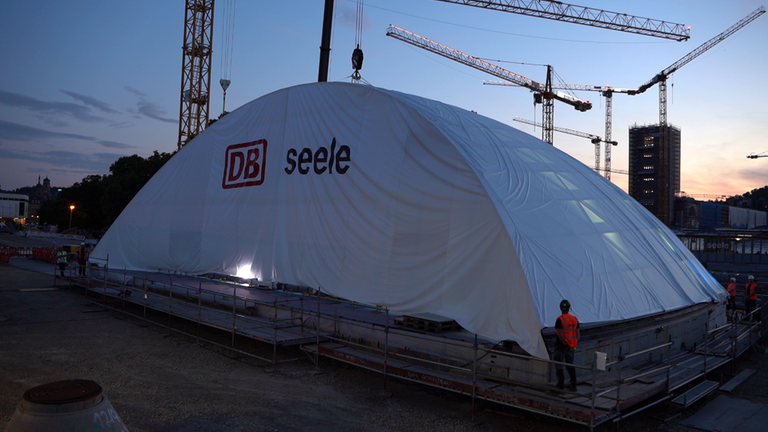 Eine weiße Plane verdeckt noch die große Halbkugel, durch die Reisende später in die Tiefbahnhofshalle treten können.