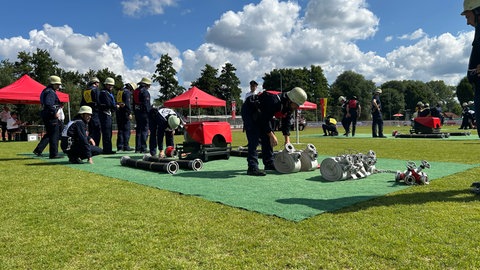 Zwei Feuerwehrleute machen sich bereit Schläuche zu verlegen. In unterschiedlichen Disziplinen treten sie gegeneinander an. Ziel des Wettbewerbs ist es die Feuerwehrmänner und -frauen auf den Ernstfall vorzubereiten und den Teamgeist zu stärken.