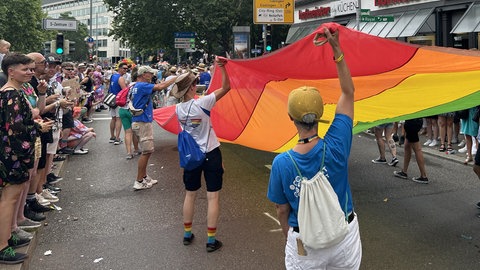 Menschen halten eine riesige Regenbogenfahne beim CSD 2024 in Stuttgart.