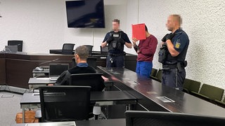 Der Angeklagte im Mordprozess hält sich einen Ordner vor das Gericht.