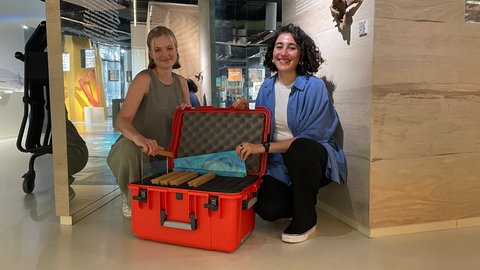 Alles Material in einem roten Koffer: Hannah Allgayer (links) und Makisa Fathai (rechts) stellen Bibliorama ihr Dialog-Projekt vor. 