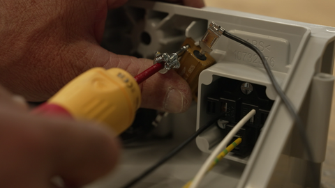 Mit einem kleinen Schraubenzieher befestigt ein Mann ein Schraube an einem elektronischen Gehäuse. 