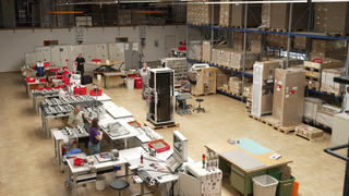 Der Blick in eine Arbeitshalle der Elektrofirma Intec in Besigheim mit Tischen, Kartons, Mitarbeitern und Elektrogeräten. 