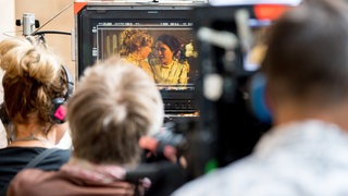 Mitglieder einer Filmcrew betrachten auf dem Monitor gedrehte Filmszene