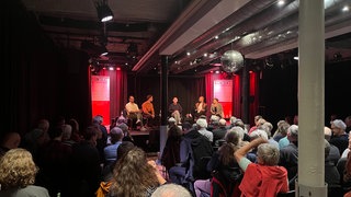 Bei einer Podiumsdiskussion sitzen Menschen in Stuttgart auf einer Bühne. 