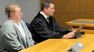 Eine Angeklagte sitzt neben ihrem Rechtsanwalt im Saal des Amtsgerichts Stuttgart, weil sie für einen Stadtbahnunfall im Februar 2024 verantwortlich sein soll. 