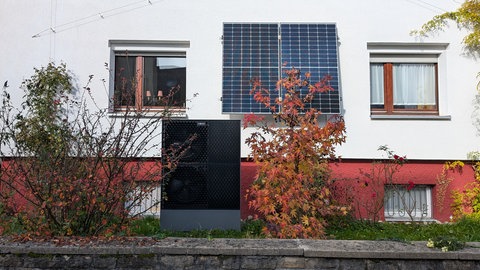 Wärmepumpe vor Privathaus zwischen herbstlichen Sträuchern