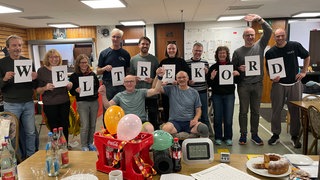 Eine Gruppe hält die Einzelbuchstaben des Begriffs Weltrekord vor dem Körper und umrahmt damit die beiden Kegel-Weltmeister in Stuttgart.