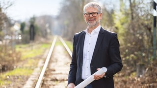 Michael Ilk mit Bahngleisen im Hintergrund und einer großen Papierrolle