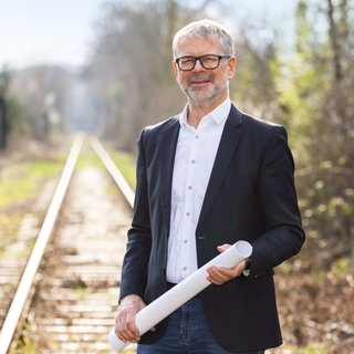 Michael Ilk mit Bahngleisen im Hintergrund und einer großen Papierrolle