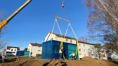 Wärmepumpe wird von einem Kran vor ein Wohnhaus positioniert