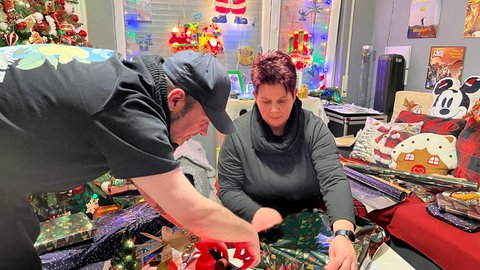 Denis Kegreiß und eine Helferin aus der Nachbarschaft verpacken Weihnachtsgeschenke.