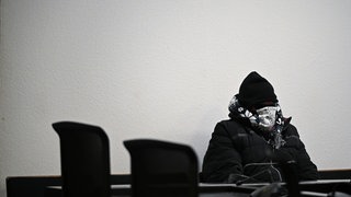 Ein angeklagter Polizist sitzt vor Prozessbeginn vermummt in einem Gerichtssaal im Landgericht Stuttgart. 