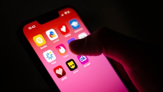 Eine Hand hält ein Smartphone mit verschiedenen Dating-Apps auf dem Bildschirm 