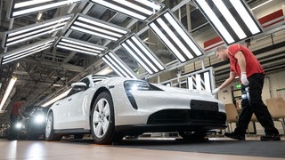Ein Mitarbeiter der Porsche AG führt in einer Produktionshalle des Porsche-Stammwerks die Sichtprüfung eines Porsche Taycan durch. 