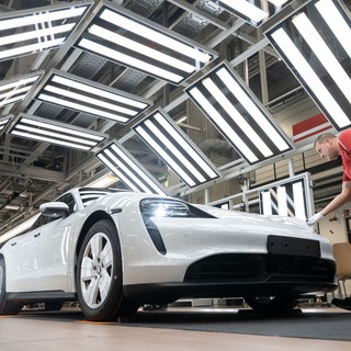 Ein Mitarbeiter der Porsche AG führt in einer Produktionshalle des Porsche-Stammwerks die Sichtprüfung eines Porsche Taycan durch. 