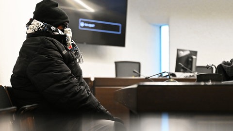 Ein Angeklagter sitzt mit Schal, Mütze und Sonnenbrille vermummt in einem Gerichtssaal im Landgericht Stuttgart. Dem Polizeibeamten aus Fellbach wird vorgeworfen, die Mafia um eine "Abreibung" für seinen Vorgesetzten gebeten zu haben.