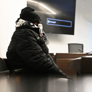 Ein Angeklagter sitzt mit Schal, Mütze und Sonnenbrille vermummt in einem Gerichtssaal im Landgericht Stuttgart. Dem Polizeibeamten aus Fellbach wird vorgeworfen, die Mafia um eine "Abreibung" für seinen Vorgesetzten gebeten zu haben.