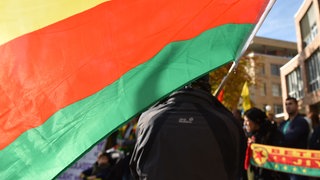 Die Flagge der nordsyrischen Autonomen Kurdenregion Rojava wird bei einer Kundgebung von Kurden in Stuttgart von einem Mann in der Hand gehalten. (Symbolbild)