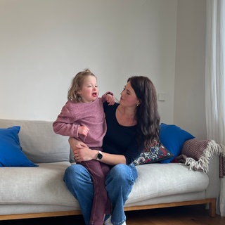 Noemi mit ihrer Mutter auf dem Sofa: Die Neunjährige kann derzeit nicht zur Schule, weil die Stadt Stuttgart den Vertrag mit dem Träger für die Eingliederungshilfe gekündigt hat.