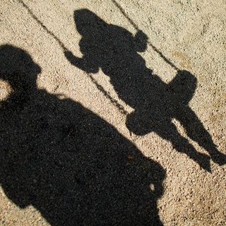 Der Schatten von einem Mann und einem schaukelnden Kind sind im Sand auf einem Spielplatz zu sehen. Ein Tagesvater im Rems-Murr-Kreis soll Kinder schwer sexuell missbraucht haben.