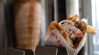 Ein Döner Kebap auf einer Theke, im Hintergrund ein Drehspieß (Symbolbild)