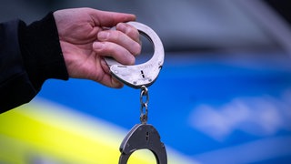 Symbolbild: Handschellen vor Polizeiauto im Zusammenhang mit Seriendiebstahl von Autoteilen in Stuttgart