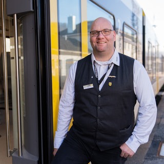 Ronald-Phillip Tolkiehn steht vor einem Zug von Arverio. Der Zugbegleiter ist von "Allianz pro Schiene" als "Eisenbahner des Jahres 2026" ausgezeichnet worden.