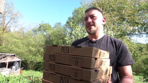 Ein Mann trägt mehrere Pizzakartons. 