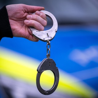 Ein Polizist hält ein Paar Handschellen. (Symbolbild)