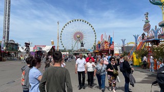 Menschen schlendern beim Frühlingsfest in Stuttgart über den Cannstatter Wasen.