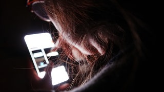 Eine junge Frau bedient ihr Smartphone im Dunkeln.