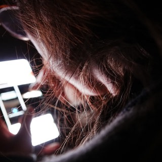 Eine junge Frau bedient ihr Smartphone im Dunkeln.
