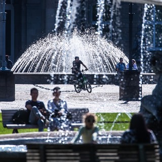 Menschen sitzen bei Sonnenschein an den Springbrunnen am Stuttgarter Schlossplatz. (Archivbild)