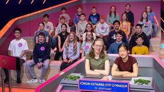 Die "erste Reihe Kids" Mathilda Enste und Riqui Liu sitzen im Quizstudio vor ihren Klassenkameradinnen und Kameraden.