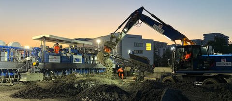 A81-Ausbau: Ein Bagger schaufelt Beton vor den Betonfertiger. 