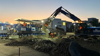 A81-Ausbau: Ein Bagger schaufelt Beton vor den Betonfertiger. 