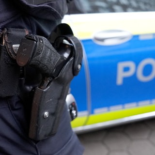 Symbolbild zu einem Polizeieinsatz mit Waffe und Polizeiwagen.
