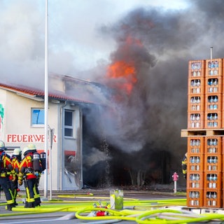 Feuerwehrleute stehen vor dem brennenden Gerätehaus der Feuerwehr Unterensingen.