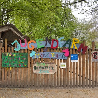 Eingang der Jugendfarm Möhringen-Vaihingen in Stuttgart mit buntem Holzschild, Öffnungszeiten und dem Hinweis auf eine handyfreie Zone.