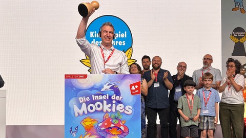 Brettspiel-Autor Florian Sirieix jubelt in Berlin auf der Bühne bei der Verleihung des "Kinderspiel des Jahres 2026": Mit "Die Insel der Mookies", erschienen beim Verlag Kosmos aus Stuttgart, siegte erstmals ein Zwei-Personen-Spiel in dieser Kategorie.
