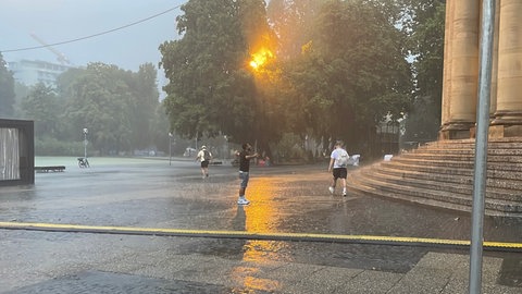 Nach Tagen der Hitze endlich Abkühlung: Ein junger Mann freut sich auf dem Platz vor der Oper in Stuttgart über den Regen.