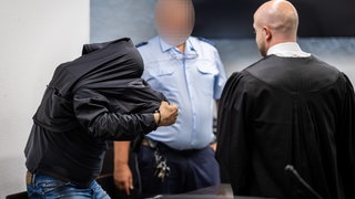 Ein Angeklagter geht in einem Gerichtssaal des Landgerichts Stuttgart zu seinem Platz. Der wegen Totschlags angeklagte Mann soll eine Frau zwischen Ende Juli und Anfang August 2025 umgebracht haben und die Leiche anschließend in einen Rollkoffer verpackt haben.
