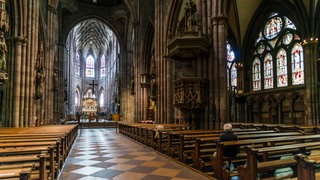 Der Kirchenraum des Freiburger Münsters, ein paar Gläubige sitzen auf den Bänken.