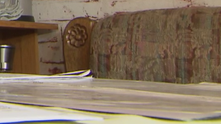 Mann mit längerem Bart sitzt neben vielen Blättern am Schreibtisch.