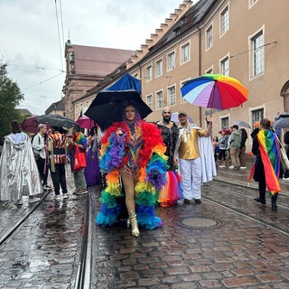Mehrere Menschen in Regenbogenfarben gekleidet und mit Regenbogen-Schirmen.